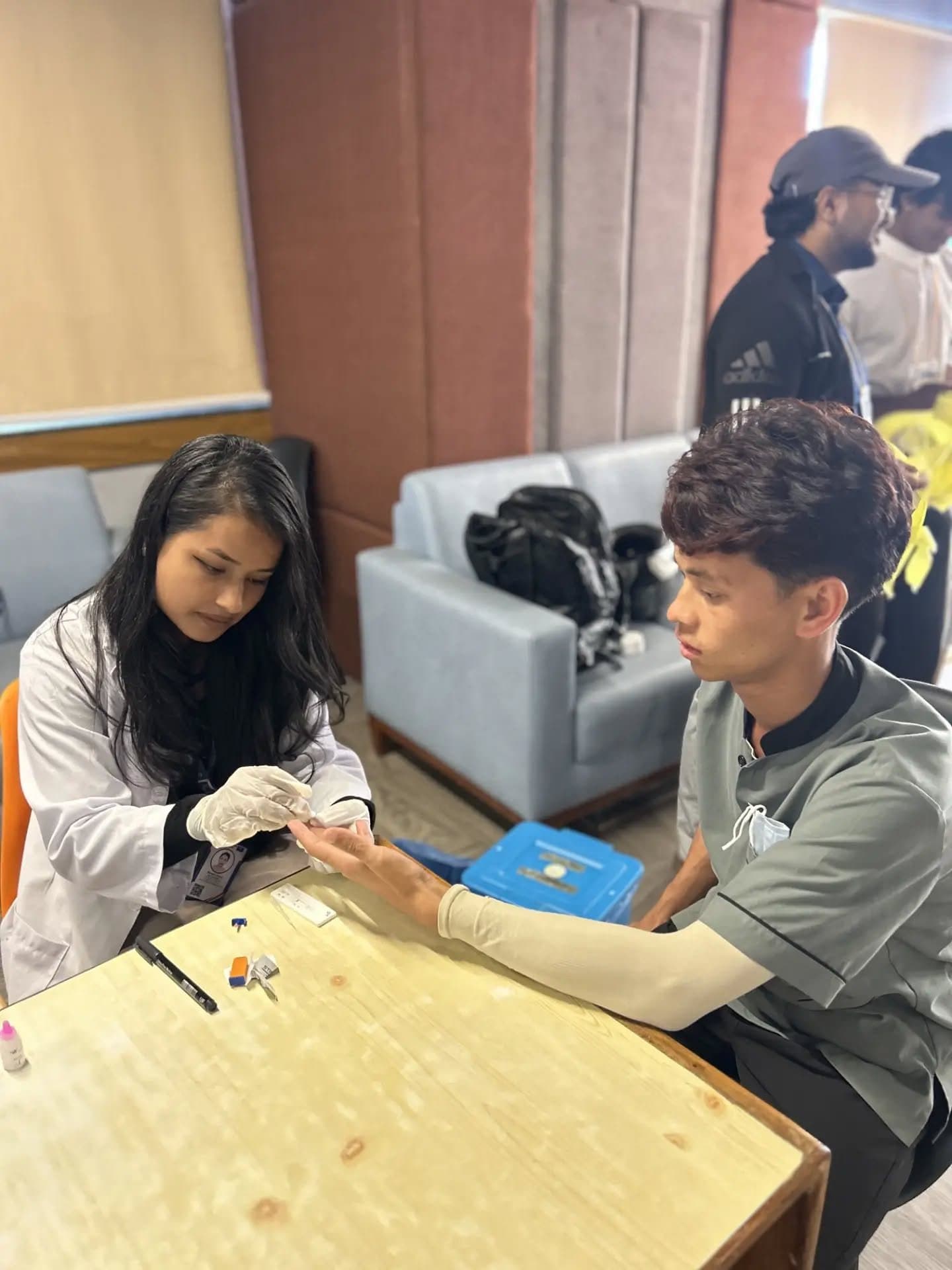 A Leo volunteer runs a finger-prick blood test for a visitor at a health screening camp.