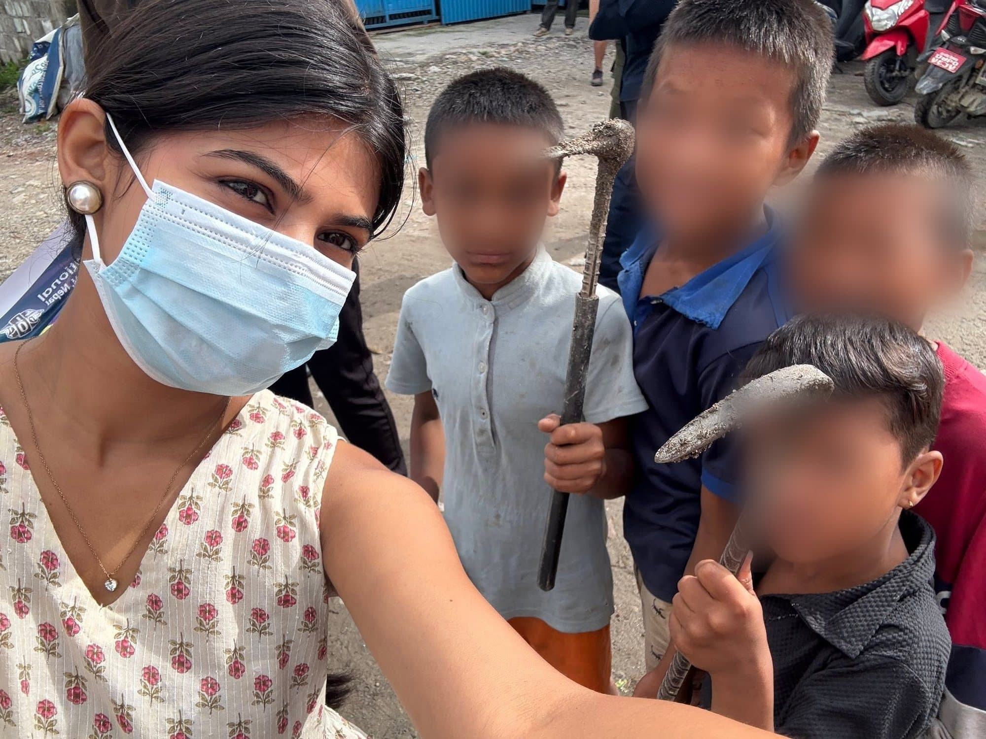 A masked Leo volunteer with a group of children holding tools during a neighbourhood clean-up.